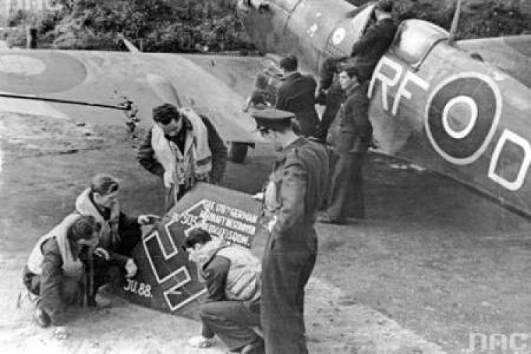 Lotnicy dywizjonu 303 oglądają szczątki zestrzelonego niemieckiego junkersa. Z prawej „Spitfire” Jana Zumbacha Fot. NAC
