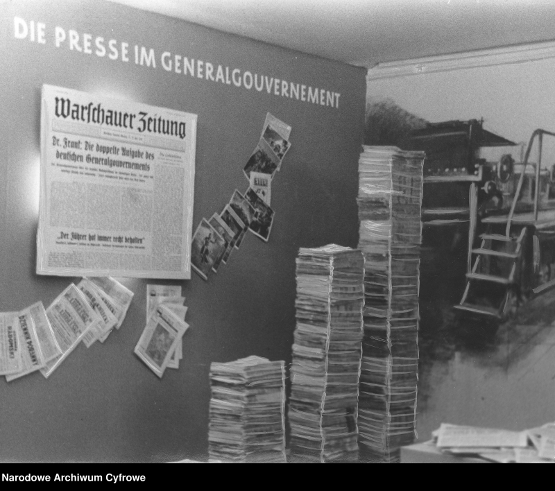 Niemieckie Targi Wschodnie w Królewcu w 1940 r. Fragment ekspozycji. Widoczna m.in. maszyna drukarska oraz poukładane stosy gazet. Na ścianie egzemplarz "Warschauer Zeitung". Fot. Narodowe Archiwum Cyfrowe