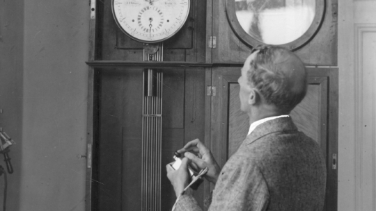 Pracownik obserwatorium stojący przy zegarze, który jest połączony kablem podziemnym z zegarem regulacyjnym w Ministerstwie Komunikacji. - 1932 r. Źródło: NAC