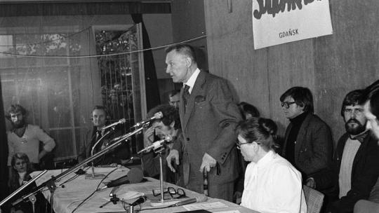 Konferencja prasowa gdańskiej „Solidarności”: przemawia Lech Bądkowski, rzecznik prasowy „S”; przy stole z lewej Bogdan Lis, z prawej Anna Walentynowicz; z tyłu Andrzej Celiński (3P). Gdańsk, 31.10.1980. Fot. PAP/CAF/S. Kraszewski