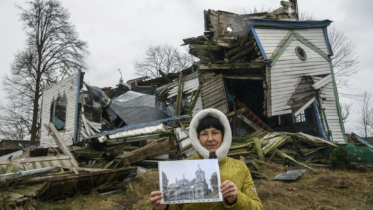 Olena Panina pokazuje, jak wyglądał kościół Narodzenia Najświętszej Maryi Panny we wsi Wiazówka w obwodzie żytomierskim na Ukrainie przed rosyjskim bombardowaniem w marcu 2022 r. XIX-wieczny drewniany kościół Narodzenia Najświętszej Maryi Panny to zabytek architektury o znaczeniu narodowym. Fot. PAP/V. Musiienko
