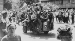 Radomski Czerwiec 1976 - grupa młodych ludzi jadących akumulatorowym wózkiem z narodową flagą przed gmach KW PZPR. Fot. PAP/CAF/Reprodukcja