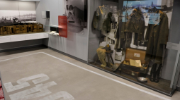 Fragment jednej z wystaw stałych w Muzeum w Łambinowicach. Prawą stronę zajmuje gablota, w której znajdują się elementy umundurowania żołnierskiego. Z lewej strony drewniana makieta baraku, w którym przetrzymywano jeńców wojennych. Fot. MKiDN