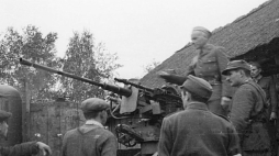 Grupa Kampinos podczas Powstania Warszawskiego: Major Alfons Kotowski ps. „Okoń” przemawia do żołnierzy zgrupowania „Kampinos” przed wymarszem do lasów świętokrzyskich. Obok zdobyczne działko przeciwlotnicze 2 cm FlaK 38 ze sprzężonym karabinem maszynowym. Poniżej z prawej stoi porucznik Adolf Pilch ps. „Dolina” (w rogatywce), odwrócony plecami z opaską na ramieniu podporucznik Lech Zabierek ps. „Wulkan”. Druga połowa września 1944 r. Źródło: Wikimedia Commons