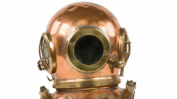 Hełm nurkowy Siebe-Gorman 6-bolcowy z kołnierzem. Na przedniej płaszczyźnie kołnierza widoczne bolce do zawieszania zaczepów od ciężarków. Poniżej tabliczka znamionowa z nazwą producenta Siebe-Gorman & Company Ltd. Elementy zestawu nurkowego Siebe-Gorman. Fot. P. Jóźwiak | Zbiory NMM