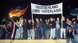 Zdjęcie z 22 grudnia 1989 r. przedstawia dużą grupę mieszkańców Berlina stojących na Murze Berlińskim. Trzymają oni niemiecką flagę oraz transparent z napisem „Niemcy – Zjednoczona Ojczyzna”. Fot. EPA/STR Dostawca: PAP/EPA