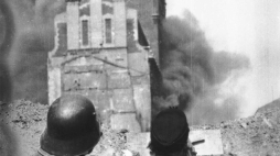 Powstańcy z baonu „Kiliński” na barykadzie na ul. Zielnej obserwują płonący gmach PAST-y. Źródło: Wikimedia Commons