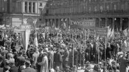 Uczestnicy pochodu na placu Teatralnym. Widoczna m.in. tablica z napisem BOS (Biuro Odbudowy Stolicy) i transparenty "zwycięstwo!", "koniec wojny, początek odbudowy". W głębi Teatr Wielki. /NAC