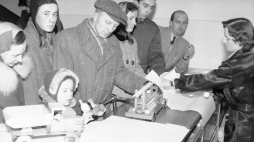 Sprzedawczyni pakująca zakupioną zabawkę. Na ladzie stoją: drewniany samochód strażacki oraz ciężarowy. Widoczni klienci oglądający zabawki, lata 1950 - 1960. /NAC