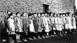 Więźniarki na apelu, stojące na tle ceglanego baraku. Za nimi nadzorczyni Eugenia Pohl – obóz przy ul. Przemysłowej w Łodzi, wiosna 1944 r. Źródło: IPN w Łodzi
