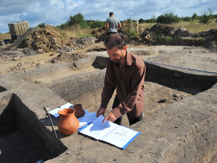 Prowadzący badania archeolog Marcin Dziewanowski pokazuje repliki glinianych garnków podczas prac archeologicznych w Stobnie. Fot. PAP/M. Bielecki