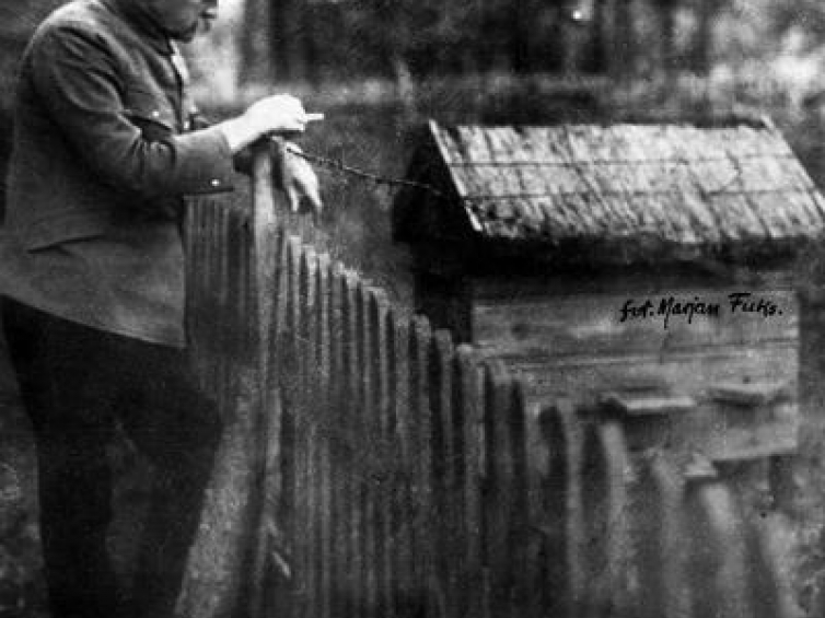 Józef Piłsudski pali papierosa oparty o płot. Źródło: NAC