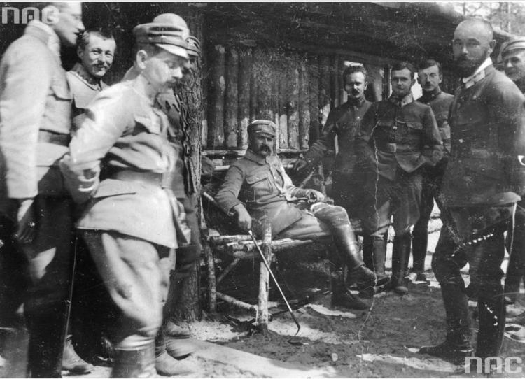 Brygadier Józef Piłsudski (siedzi w środku) w towarzystwie oficerów I Brygady Legionów Polskich. Widoczni m.in.: pułkownik Edward Rydz-Śmigły (z prawej na pierwszym planie), porucznik Bolesław Wieniawa-Długoszowski (za E. Rydzem-Śmigłym), major Michał Żymierski (stoi 2. z lewej na drugim planie, z rękami w kieszeniach). Źródło: NAC