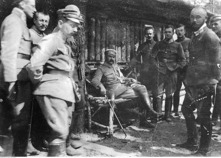 Wołyń, 1916 r. Oficerowie I Brygady Legionów Polskich: brygadier Józef Piłsudski (siedzi w środku) w towarzystwie oficerów I Brygady Legionów Polskich. Widoczni m.in.: płk Edward Rydz-Śmigły (z prawej na pierwszym planie), por. Bolesław Wieniawa-Długoszowski (za E. Rydzem-Śmigłym), mjr Michał Żymierski (stoi 2. z lewej na drugim planie, z rękami w kieszeniach). Źródło: NAC