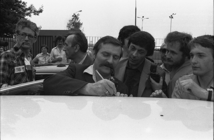 Warszawa, 1981-06-08. Lech Wałęsa wraca z dorocznej konferencji Międzynarodowej Organizacji Pracy w Genewie, 5 czerwca 1981 r. wygłosił entuzjastycznie przyjęte przemówienie, relacjonowane przez wszystkie telewizje zachodnioeuropejskie. Nz. przed halą przylotów na Okęciu Lech Wałęsa (C) daje autograf chłopcu, kartkę położył na dachu samochodu. Z lewej dziennikarze Tygodnika Solidarność: Krzysztof Wyszkowski (L) i Tadeusz Mazowiecki (2L) - red. naczelny pisma. Fot. PAP/CAF/A. Rybczyński