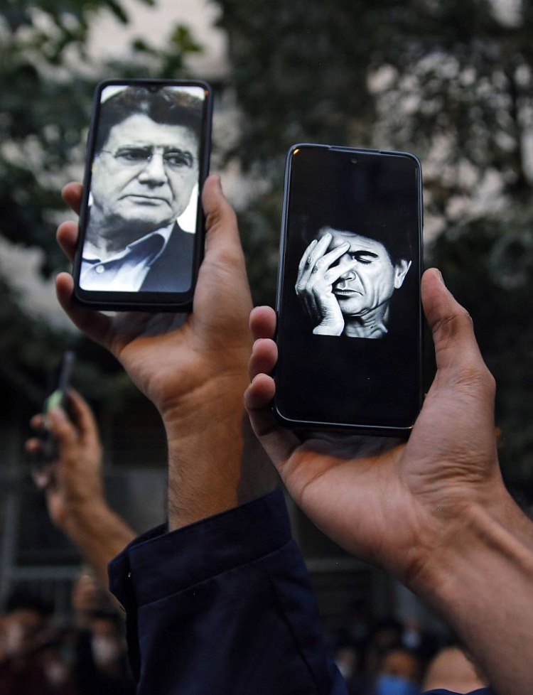 Mohammad Reza Szadżarian na ekranach telefonów osób zgromadzonych przed szpitalem, w którym zmarł artysta. Fot. PAP/EPA