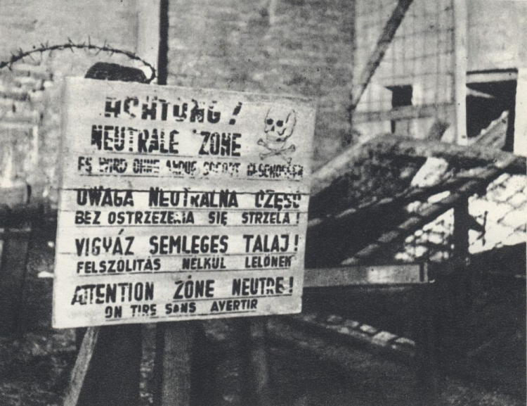 Wielojęzyczna tablica ostrzegawcza przy ogrodzeniu niemieckiego obozu koncentracyjnego KL Warschau. Źródło: Wikimedia Commons