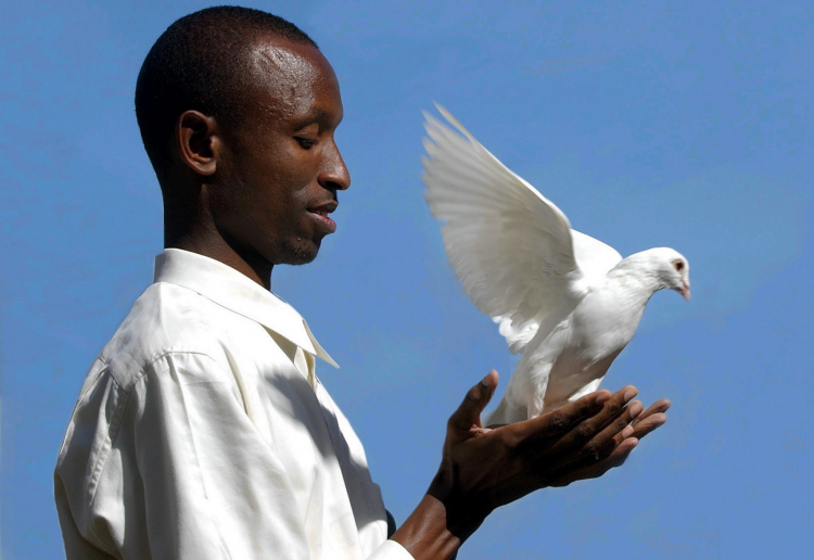 Gilbert Mwenedata, który przeżył masakrę swych ziomków w Rwandzie, wypuszcza gołębia.  PAP/EPA /Julian Smith