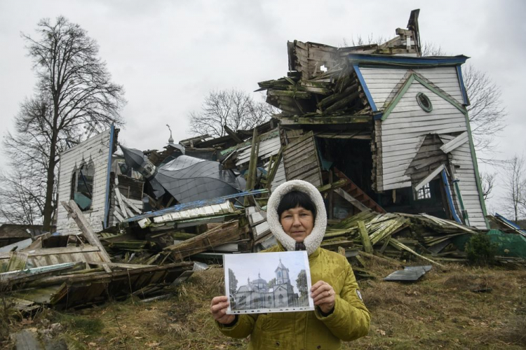 Olena Panina pokazuje, jak wyglądał kościół Narodzenia Najświętszej Maryi Panny we wsi Wiazówka w obwodzie żytomierskim na Ukrainie przed rosyjskim bombardowaniem w marcu 2022 r. XIX-wieczny drewniany kościół Narodzenia Najświętszej Maryi Panny to zabytek architektury o znaczeniu narodowym. Fot. PAP/V. Musiienko