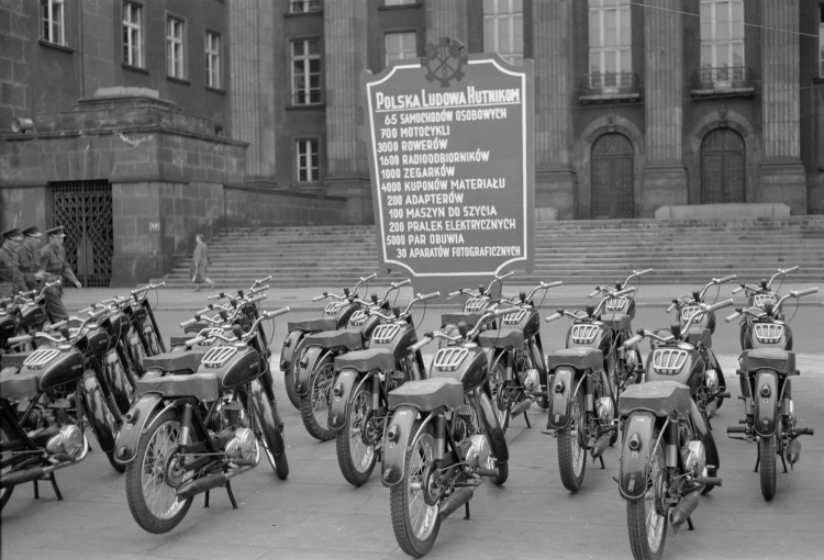 Maj 1955 r. Motocykle przeznaczone dla przodowników i racjonalizatorów hutnictwa wystawione przed Urzędem Wojewódzkim w Katowicach. Z tyłu obwieszczenie co jeszcze dostaną. Fot. PAP/CAF/Kazimierz Seko