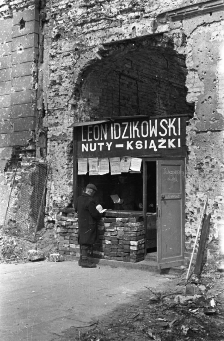 Warszawa, wiosna 1945 r. Prowizoryczna księgarnia z książkami i nutami, filia firmy wydawniczej Leona Idzikowskiego, zlokalizowana w bramie wjazdowej do zniszczonego budynku przedwojennej siedziby filii w Alejach Jerozolimskich 18. PAP/Karol Szczeciński
