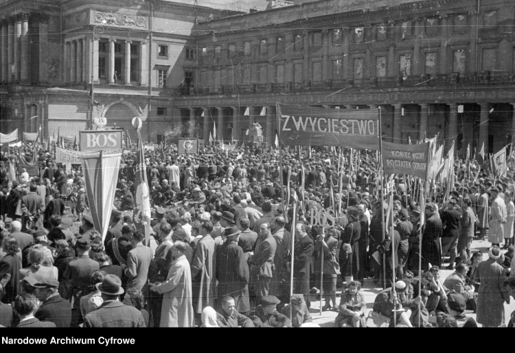 Uczestnicy pochodu na placu Teatralnym. Widoczna m.in. tablica z napisem BOS (Biuro Odbudowy Stolicy) i transparenty "zwycięstwo!", "koniec wojny, początek odbudowy". W głębi Teatr Wielki. /NAC