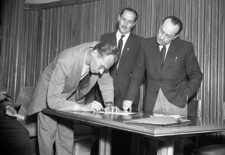 Warszawa, 1951-05-17. Literaci polscy po złożeniu 17 maja kart Narodowego Plebiscytu Pokoju podpisali deklarację pełnego zrozumienia roli pisarstwa polskiego związanego z życiem narodu i jego przyszłością. Nz. Podpis składa Jerzy Andrzejewski, obok stoją sekretarz prezydium Związku Literatów Jan Gisges i prezes Związku Literatów Leon Kruczkowski. PAP/CAF/Stanisław Dąbrowiecki