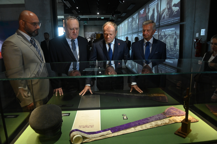 Ossów, 14 sierpnia 2025 r. Premier Donald Tusk i podsekretarz stanu w Ministerstwie Obrony Narodowej Stanisław Wziątek oraz dyrektor Muzeum Wojska Polskiego gen. dyw. w st. spocz. prof. Bogusław Pacek i dyrektor muzeum Marcin Ołdak podczas zwiedzania wystawy pt. „Zjednoczeni, niezwyciężeni” w Muzeum Bitwy Warszawskiej 1920 roku w Ossowie. Fot. PAP/Piotr Nowak