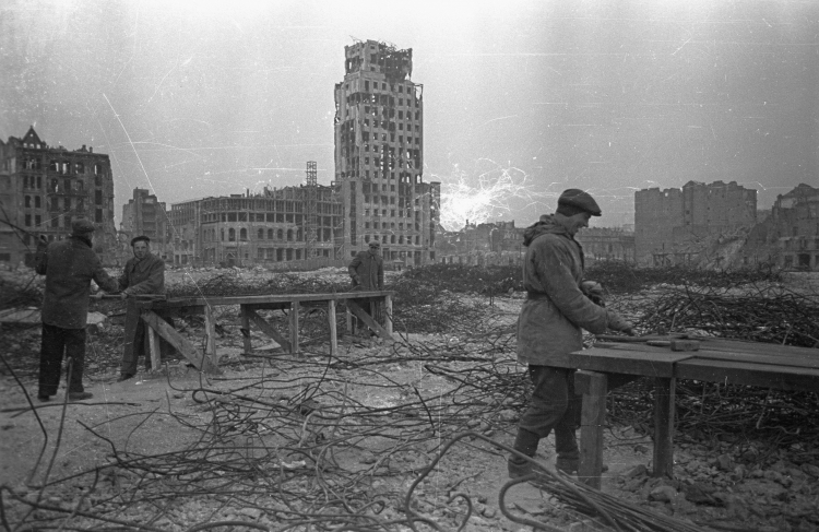 Warszawa, 1948 r. Zburzona podczas wojny zabudowa Śródmieścia. Na zdjęciu plac Napoleona ze zrujnowanym wieżowcem brytyjskiego Towarzystwa Ubezpieczeniowego Prudential. Na pierwszym planie robotnicy obrabiający pręty zbrojeniowe. Fot. PAP