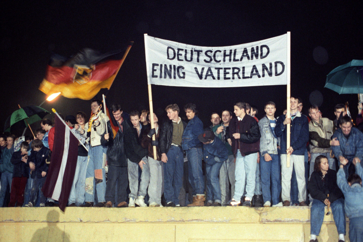 Zdjęcie z 22 grudnia 1989 r. przedstawia dużą grupę mieszkańców Berlina stojących na Murze Berlińskim. Trzymają oni niemiecką flagę oraz transparent z napisem „Niemcy – Zjednoczona Ojczyzna”. Fot. EPA/STR Dostawca: PAP/EPA
